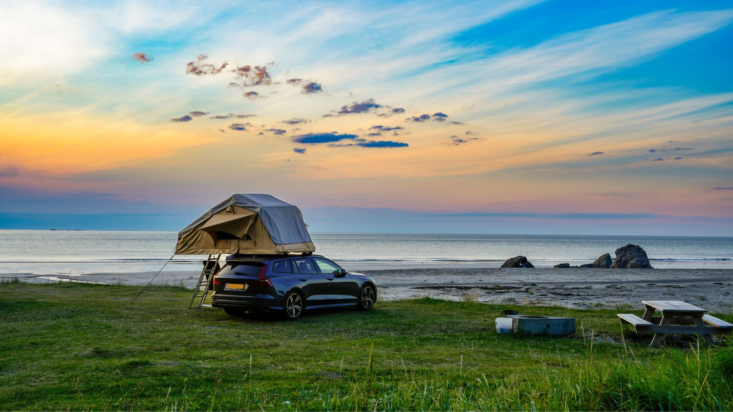 Am Meer steht ein Auto mit einem Zeltdach auf einer Wiese. Auch diese Art von Camping eignet sich gut für den Einsatz einer Trockentoilette.