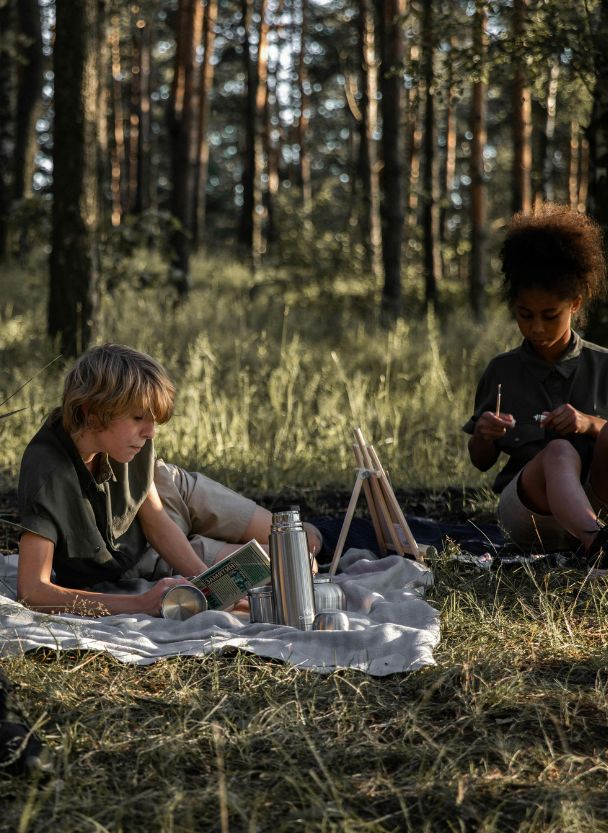 Kinder sitzen auf einer Decke im Wald und spielen. Ein idealer Ort für die Nutzung einer Komposttoilette, wenn man unabhängig sein möchte oder campen geht.