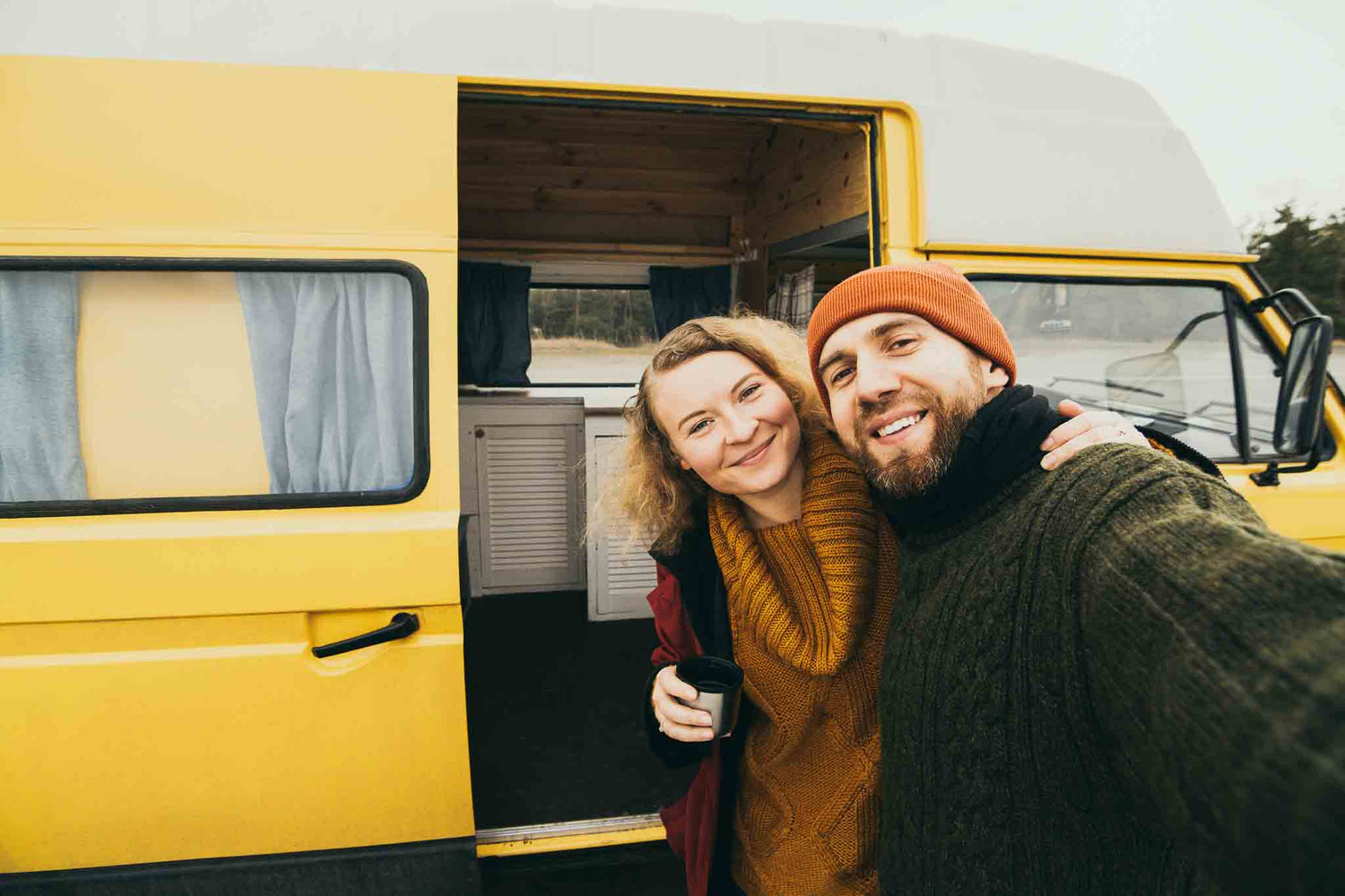 Zwei Personen stehen zusammen vor ihrem Wohnmobil und sind glücklich.