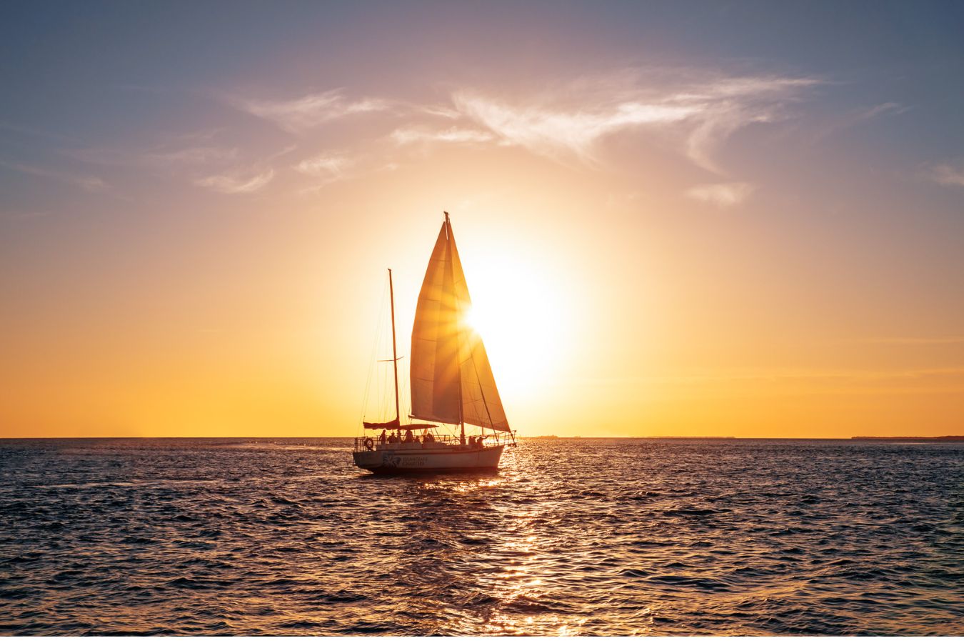 Das Bild zeigt im Sonnenuntergang ein voll besetztes Segelboot auf offenem Meer. Es spiegelt Naturliebe und Freiheit wieder und dort eignet sich eine Bordtoilette perfekt zum unabhängigen Reisen perfekt.